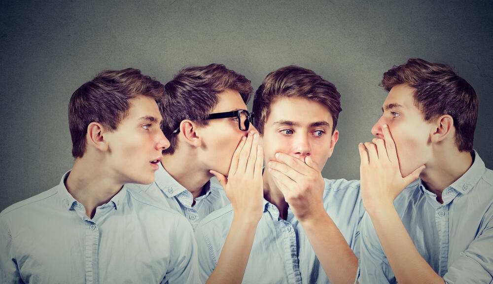 Three young men whispering each other and to shocked astonished guy in the ear. Word of mouth